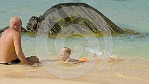 Boy swims in clear water under farther control near stones