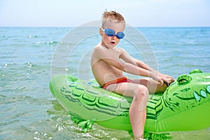 BOY SWIMS IN THE SEA ON THE CROCODYLE TOY