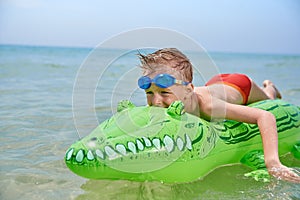 BOY SWIMS IN THE SEA ON INFLATABLE CROCODYLE TOY