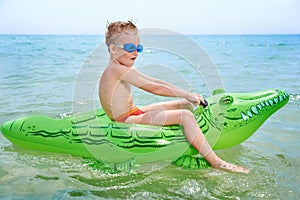 BOY SWIMS IN THE SEA ON THE INFLATABLE CROCODYLE TOY