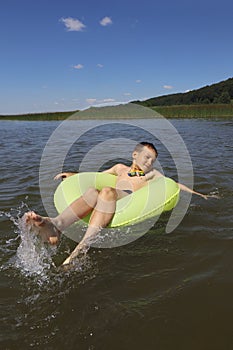 A boy swims in a yellow inflatable circle on the lake.