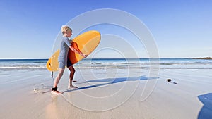 Boy in swimsuit wetsuit walk with surfboard to ocean