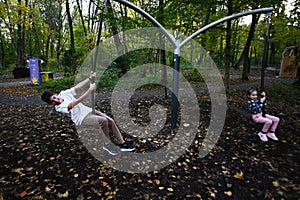 Boy swinging on a swing in an autumn park with his little sister