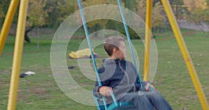 Boy swinging on swing, child having fun playing in outdoor public playground