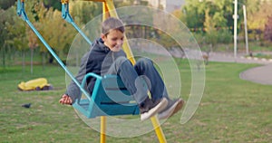 Boy swinging on swing, child having fun playing in outdoor public playground