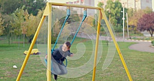 Boy swinging on swing, child having fun playing in outdoor public playground