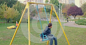 Boy swinging on swing, child having fun playing in outdoor public playground