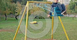 Boy swinging on swing, child having fun playing in outdoor public playground