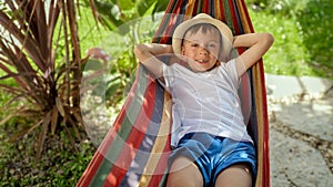 A boy swings and rests in a hammock with a smile in garden, capturing the feelings of summertime, happy childhood