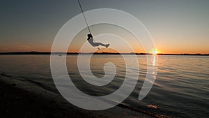 Boy swings from rope over Lake Champlain in Vermont at sunset