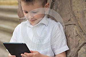 Boy with tablet near school with a book online learning