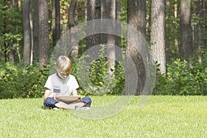 The boy with the tablet PC sitting on the grass in park. Technology, lifestyle, education, people concept