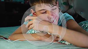 The boy takes the headphones from the bed and listens to music while lying down.