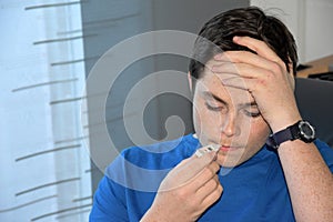 Boy takes his temperature with a  clinical thermometer