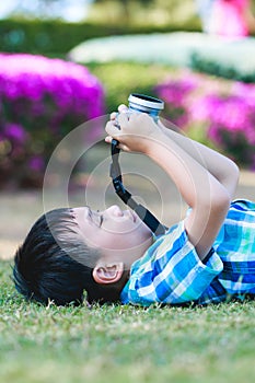 Boy taking photo by camera, exploring nature at park. Active lifestyle, curiosity, pursuing a hobby concept.