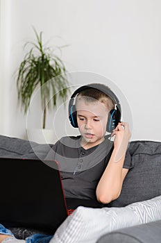 Boy talking on headphones and online video game on laptop computer at home. Child sitting and use pc