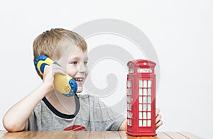 Boy talking on the phone and red telephone booth