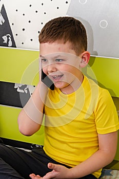 The boy is talking on the phone while sitting on his bed in his room.