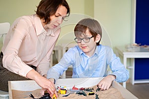 Boy with teacher is sand therapy on table light