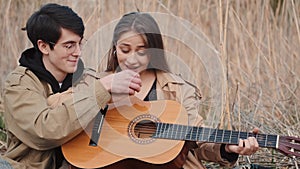 Boy teaching girl how to play song on guitar in field