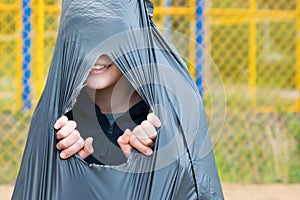 Boy tears a black trash bag from the inside, sitting in it