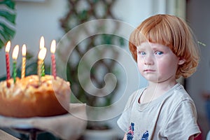 Boy with tears in his eyes can not blow out the candles on the cake