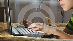 Boy teen laptop browsing internet is playing lying in bed