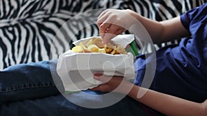 Boy teenager eating potato chips with hands on sofa at home.fast food unhealthy food