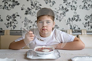 Boy teenager eating soup at kitchen table