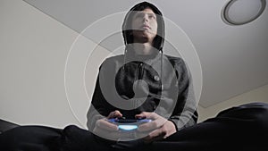 Boy teenager in the hood playing video games on the console on the gamepad. Young teen Man hooded sweater Absorbed In