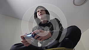 Boy teenager in the hood playing video games on the console on the gamepad. Young teen Man hooded sweater Absorbed In