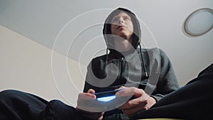 Boy teenager in the hood playing video games on the console on the gamepad. Young teen Man hooded sweater Absorbed In