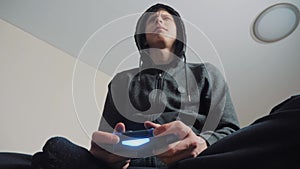 Boy teenager in the hood playing video games on the console on the gamepad. Young teen Man hooded sweater Absorbed In