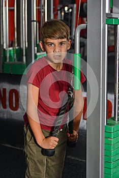 Boy teenager performs triceps exercise on the simulator in the gym. Health care from childhood