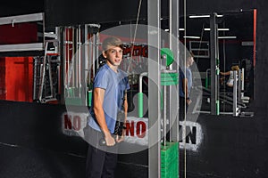 Boy teenager performs triceps exercise on the simulator in the gym. Health care from childhood