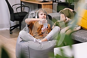 Boy teenager playing video game with joystick sitting on frameless beanbag chair