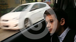 Boy teenager rides in car looking out the window. Outside the window flashed the trees and houses of the city