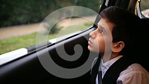 Boy teenager rides in car looking out the window. Outside the window flashed the trees and houses of the city