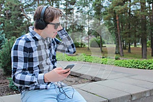 Boy teenager schoolboy or student in a shirt, smiles in glasses, listens to music on the phone