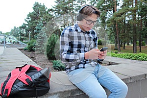 Boy teenager schoolboy or student in a shirt, smiles in glasses, listens to music on the phone