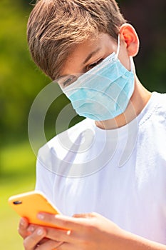 Boy teenager teen male child wearing face mask using cell phone Coronavirus COVID-19 Pandemic