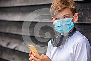 Boy teenager teen male child wearing face mask Using Phone and Headphones in Coronavirus COVID-19 Pandemic