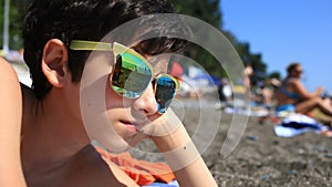 Boy a teenager wearing sunglasses on the beach, a beach with vacationers reflected in glasses.