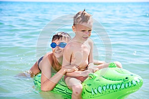 A BOY OF TEENAGERS AND LITTLE BOY IN WATER GLASSES FLOPS ON THE INFLATABLE TOY CROCODILE