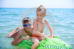 A BOY OF TEENAGERS AND A LITTLE BOY IN WATER GLASSES FLOPS ON THE INFLATABLE TOY CROCODILE