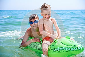 A BOY OF TEENAGERS AND A LITTLE BOY IN WATER GLASSES FLOPS ON THE INFLATABLE TOY CROCODILE