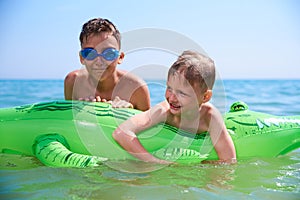 A BOY OF TEENAGERS AND A LITTLE BOY IN WATER GLASSES FLOPS ON THE INFLATABLE TOY CROCODILE