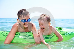 A BOY OF TEENAGERS AND A LITTLE BOY IN WATER GLASSES FLOPS ON THE INFLATABLE TOY CROCODILE