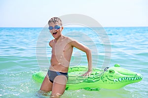 BOY OF TEENAGERS IN WATER GOGGLES SWIMS ON INFLATABLE TOY CROCODILE