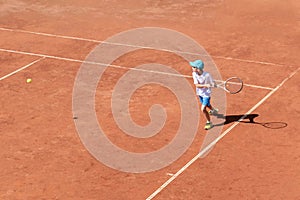 Boy tennis player plays on clay tennis court. The child is trying to hit the backhand, focused on the ball. Active games